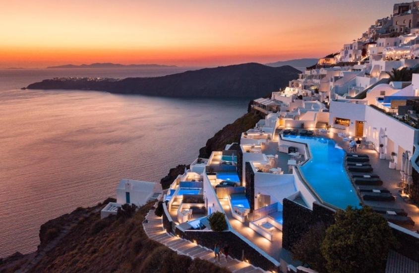 vista aérea, durante entardecer, de piscina em varanda de grace hotel santorini auberge resorts collection, hotel em montanha de para o mar em imerovigli