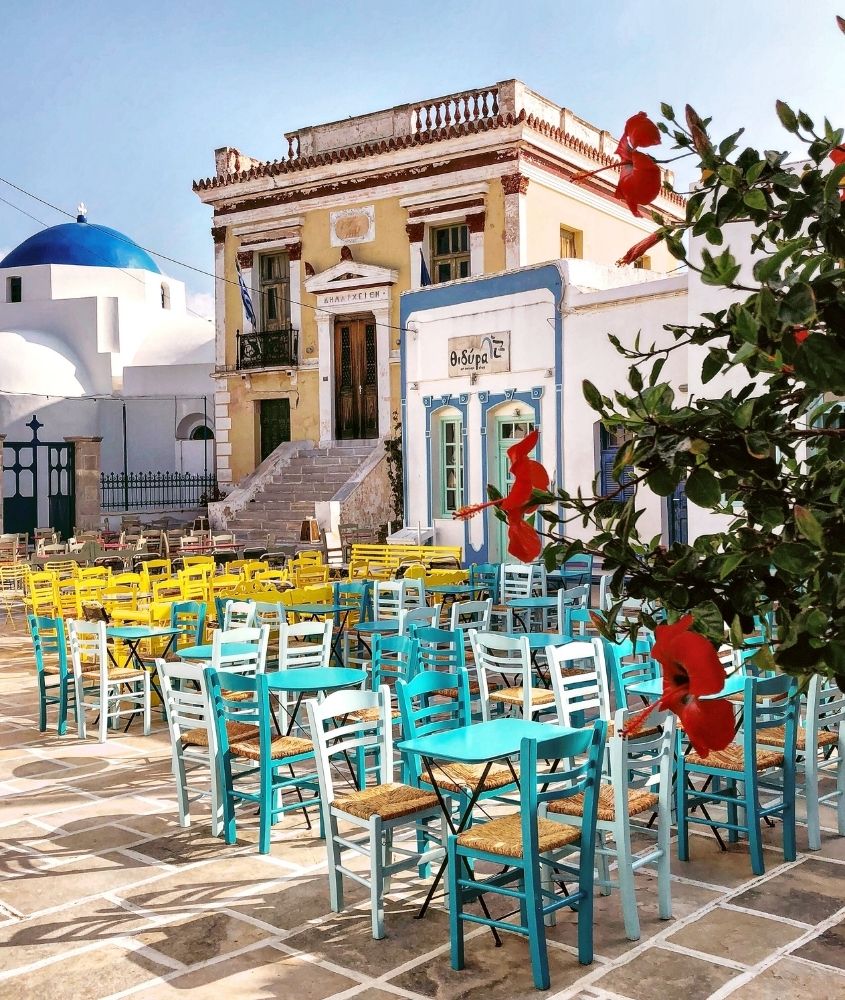 mesas e cadeiras coloridas em rua cheia de restaurantes, durante o dia, em santorini
