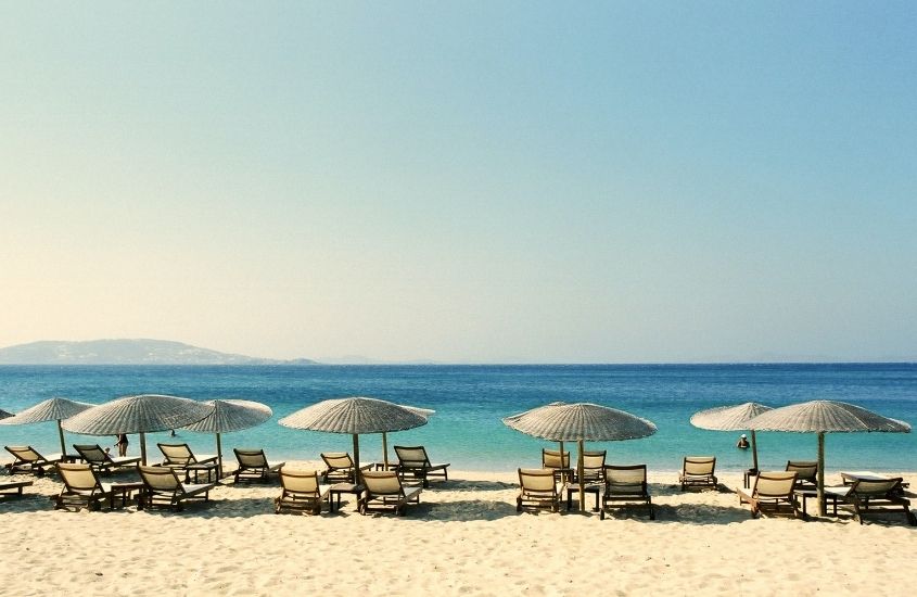cadeiras e guarda-sóis em areia de praia, durante dia ensolarado