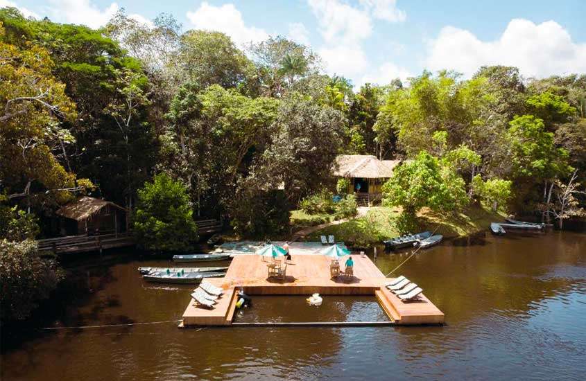 Durante um dia de sol, um dos hotéis de selva em manaus com área de lazer, espreguiçadeiras, guarda-sóis, canoas, mesas, cadeiras e floresta ao redor