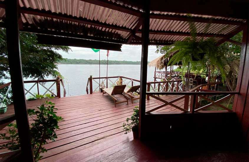 Em um dia nublado, varanda de um dos hotéis de selva no amazonas com deck de madeira, espreguiçadeiras, plantas ao redor, rio na frente e bandeiras hasteadas