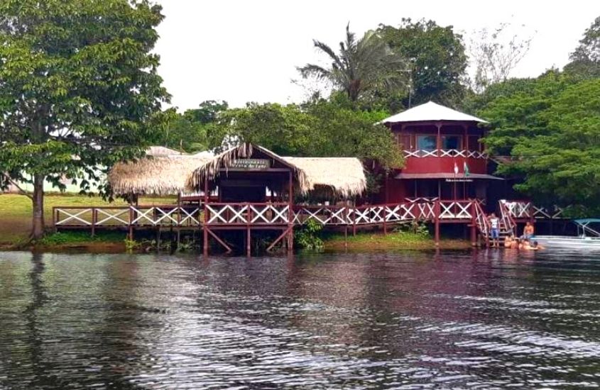 construções de palha, cercadas de árvores em frente ao rio, durante o dia em área de Vista do Lago Jungle Lodge um hotel na selva amazônica na cidade de Cajual