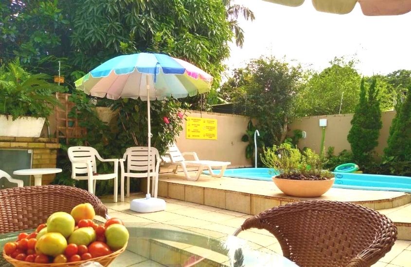 frutas em cima de mesa, em frente a piscina cercada de árvores, durante o dia, em área de lazer da Casa da Oma