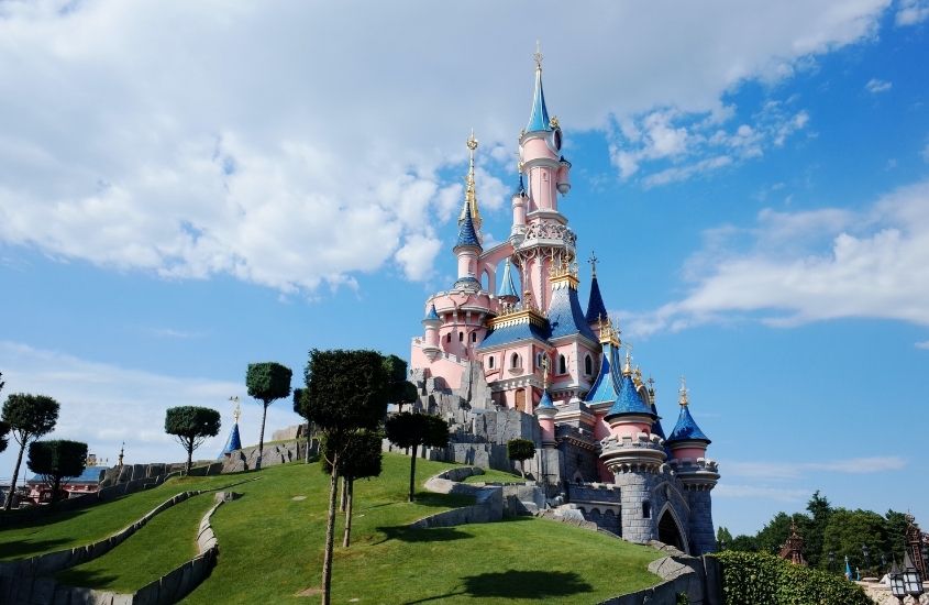 castelo rosa e azul cercado de árvores em Disneyland de paris, um dos melhores lugares para viajar com crianças
