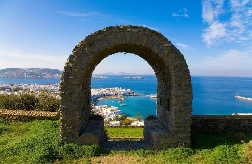 arco de pedra com vista para o mar, durante o dia, no jardim do Castle Panigirakis, patrimônio histórico e arquitetônico localizado no topo de uma montanha em mykonos