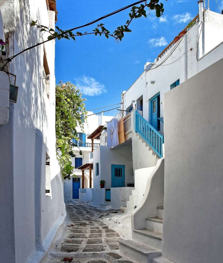 casas brancas com portas e janelas azuis, durante o dia, em rua estreita de mykonos