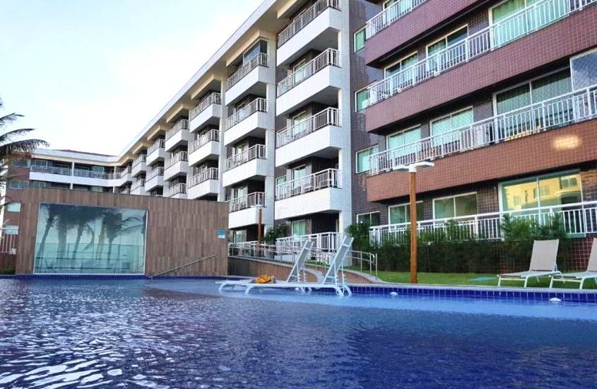 piscina em frente a prédio de apartamentos com varanda, durante o dia em apart porto das dunas