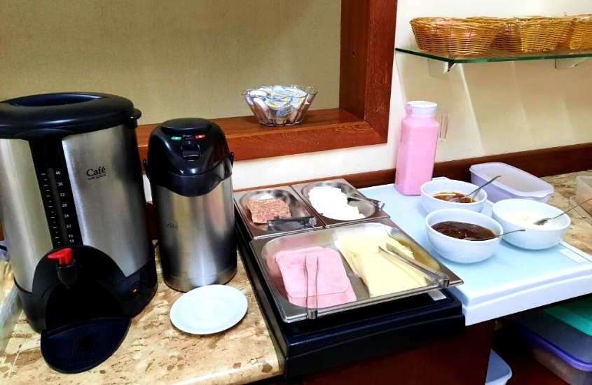 máquinas de café, presunto, queijo e molhos em cima de balcão em refeitório de hotel 3 passos