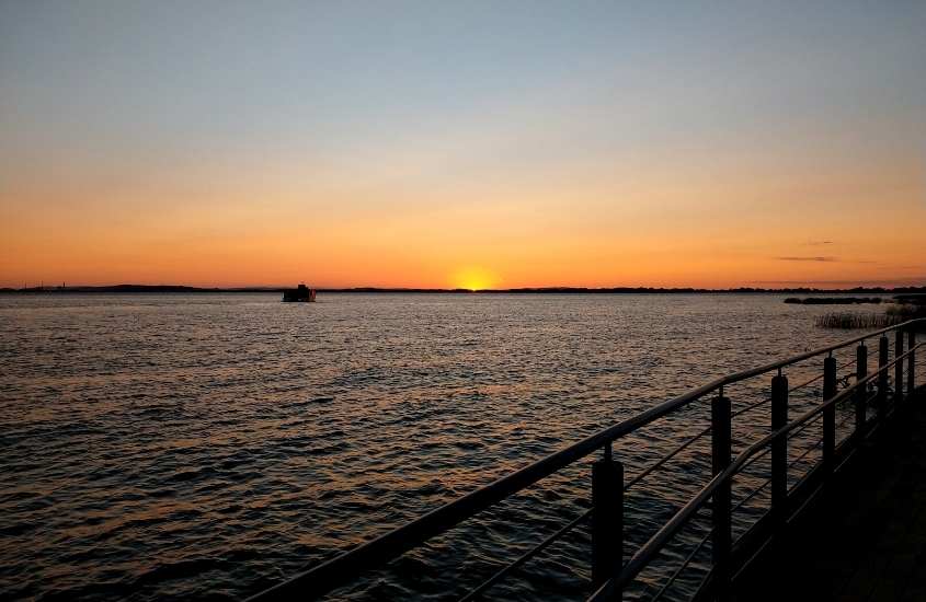 barco em alto mar, durante pôr do sol, visto da orla do guaíba