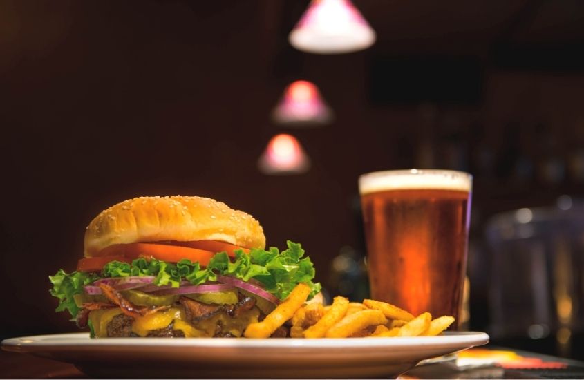 hambúrguer, batata frita e copo de cerveja em cima de mesa