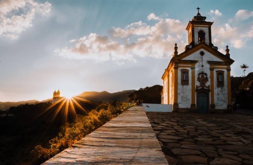 igreja branca com detalhes amarelos, em topo de morro, durante entardecer em Ouro preto, destino que é um dos melhores destinos de viagem no brasil