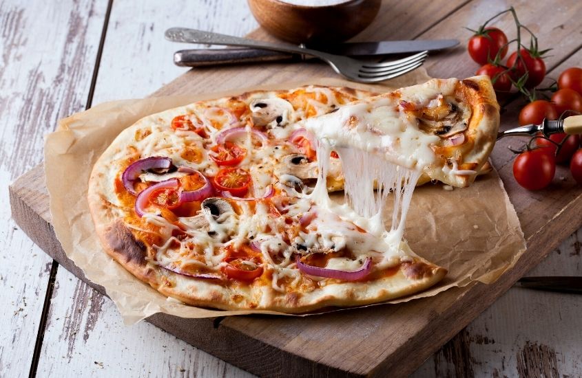 pizza com mussarela, tomate e cebola em cima de bandeja de madeira