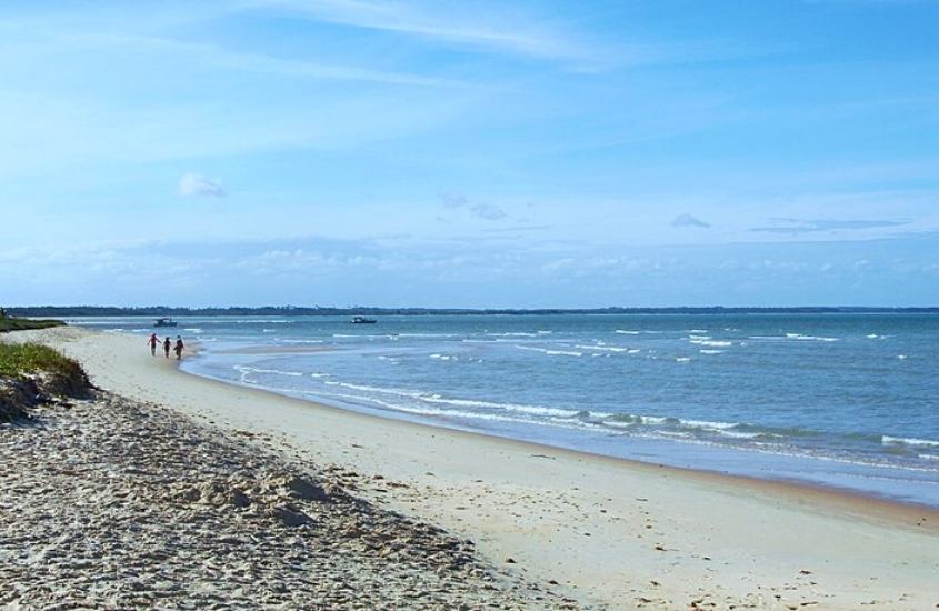 três pessoas caminham à beira-mar, durante o dia em praia