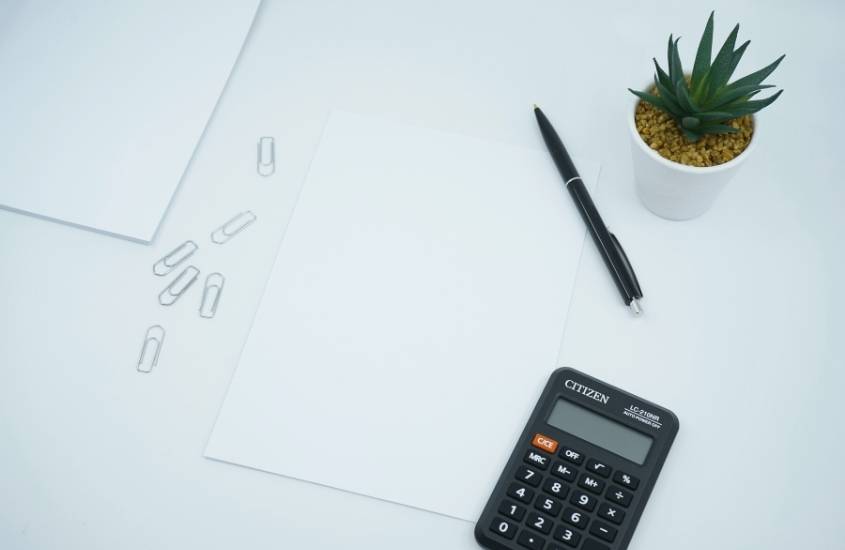 folhas de papel, clips, calculadora, caneta e vasinho de planta em cima de mesa branca