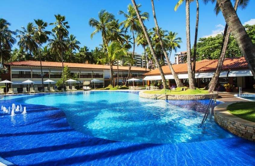 piscina cercada de espreguiçadeiras e coqueiros, durante o dia em um dos melhores hoteis em maceio, o Jatiuca Hotel & Resort