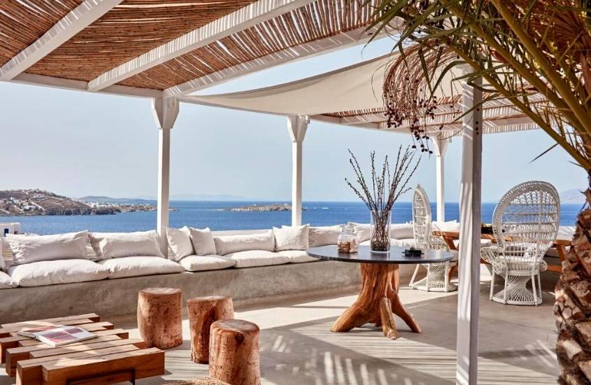 sofás, cadeiras e mesas em lounge com vista para o mar, durante o dia, em Boheme Mykonos Town, um dos melhores hoteis em mykonos
