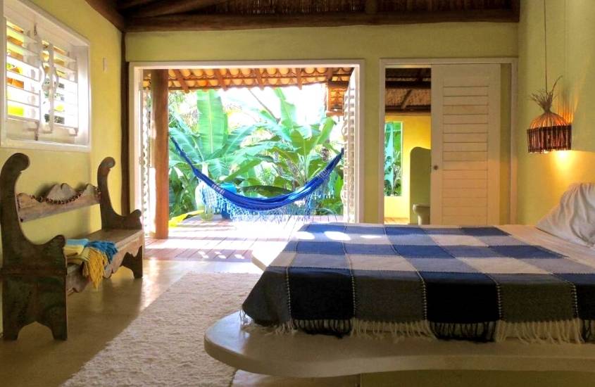 banco de madeira, cama de casal e varanda com rede de descanso em suíte de Nirvana Beach Hotel em Praia da Ponta do Mutá