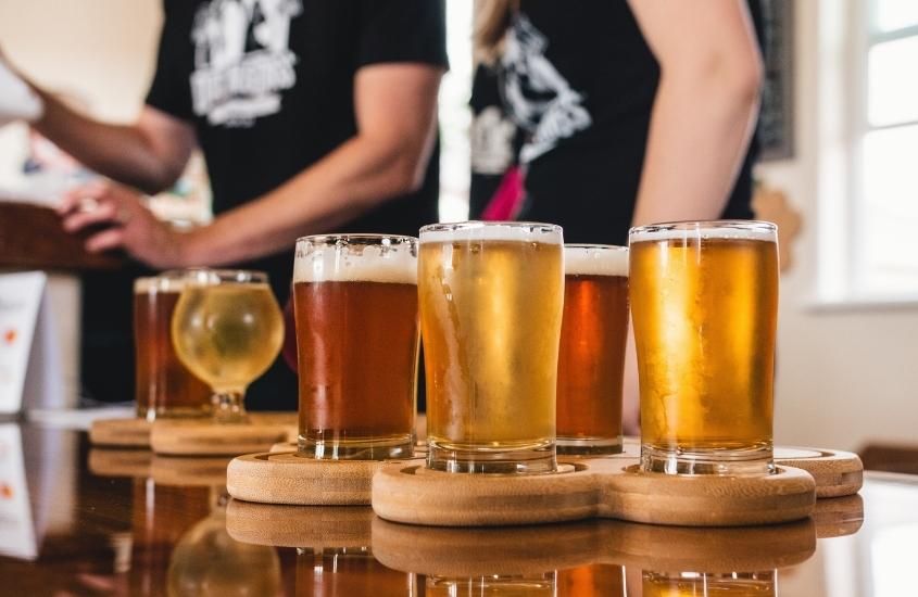diversos copos de vidro com cerveja em cima de mesa de madeira em cervejaria, uma atração para quem busca o que fazer em Garibaldi RS