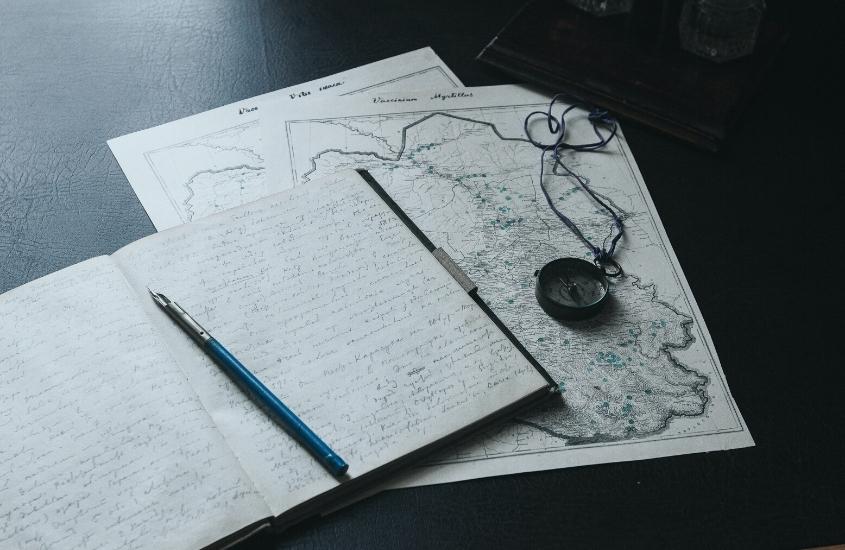 caderno de anotações, mapa e bússola em cima de mesa preta