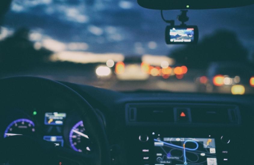 volante, gps e rádio em painel de carro e estrada embaçada vista de janela de carro durante entardecer