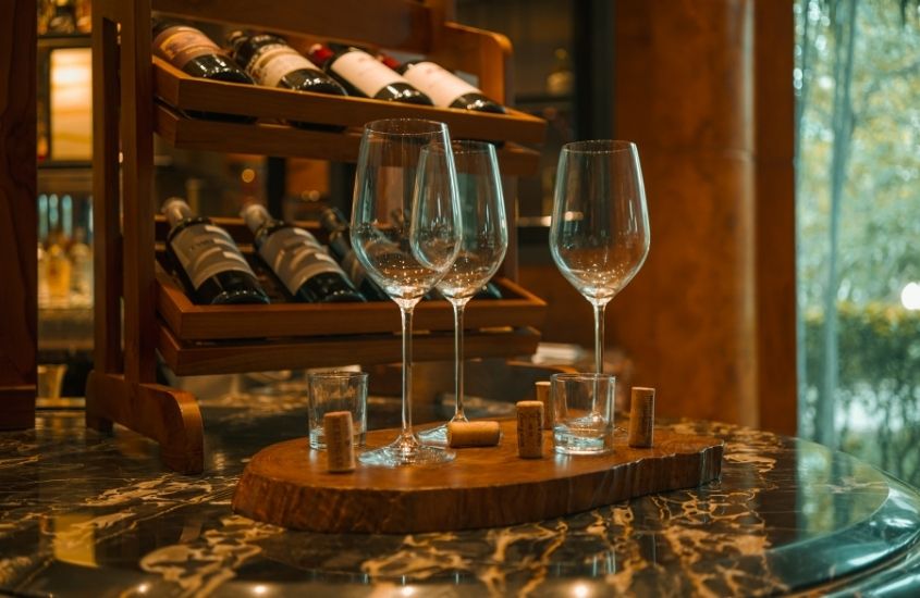 taças de vidro em cima de mesa e garrafas de vinho deitadas em prateleira em uma das vinícolas em garibaldi rs