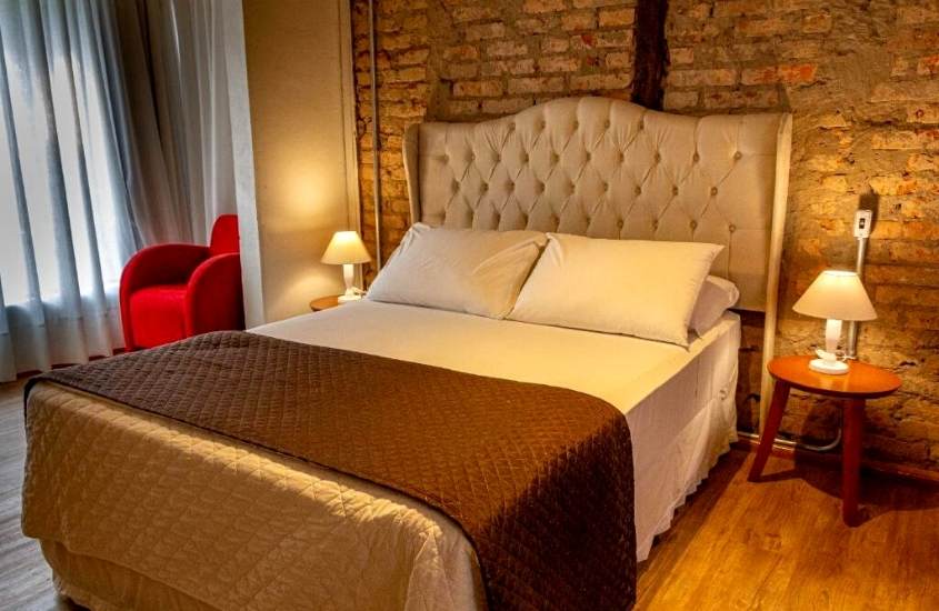 poltrona vermelha, cama de casal e abajur em cima de mesa de cabeceira em suíte de Hotel Petrópolis
