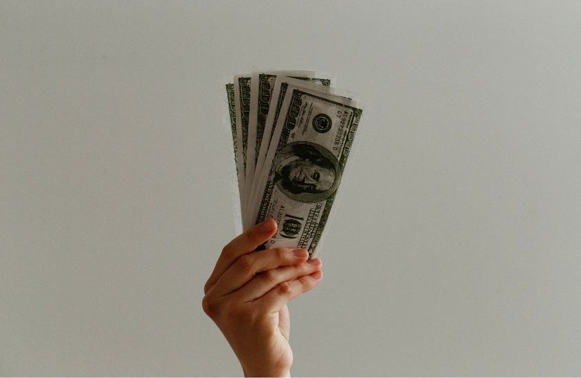 mão segurando notas de dólares em fundo branco