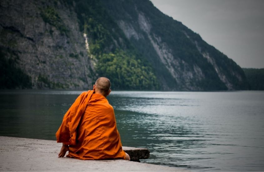monge budista, de costas, sentado em calçada em frente ao e montanha, durante o dia