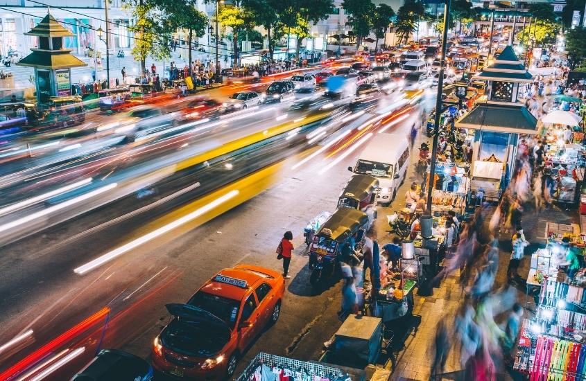 vista aérea de carros, tuk-tuks e pessoas passando em rua movimentada, cheia de barraquinhas de comida na calçada, durante a noite