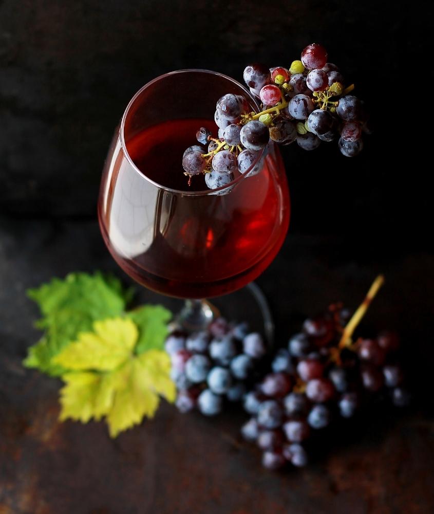 cacho de uva roxa dentro de taça de vidro com vinho
