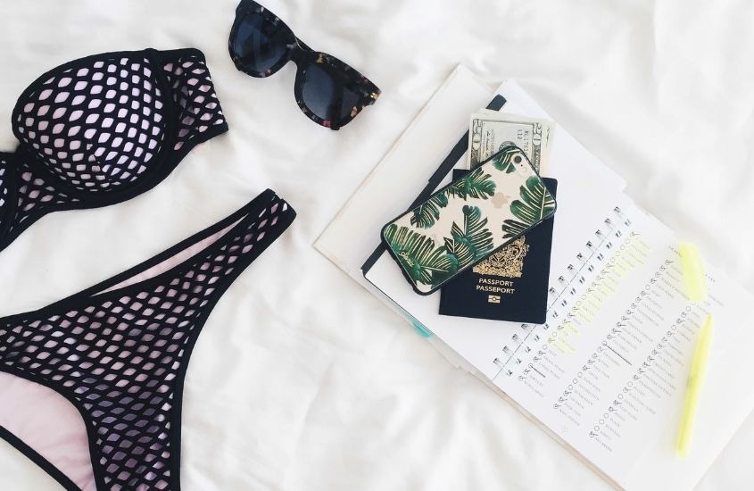 biquini, óculos de sol, caderno, celular e passaporte em cima de pano branco