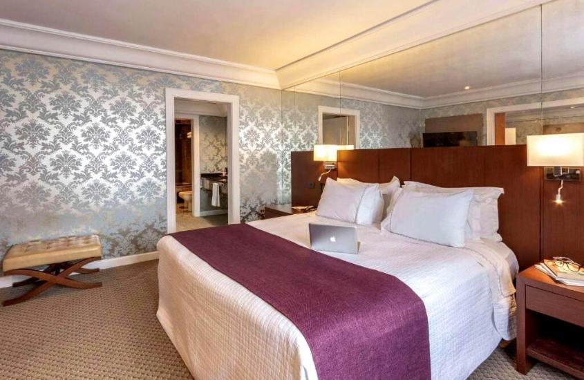 notebook prata em cima de cama de casal em suíte do Grand Mercure Curitiba, um hotel para quem procura onde ficar em curitiba