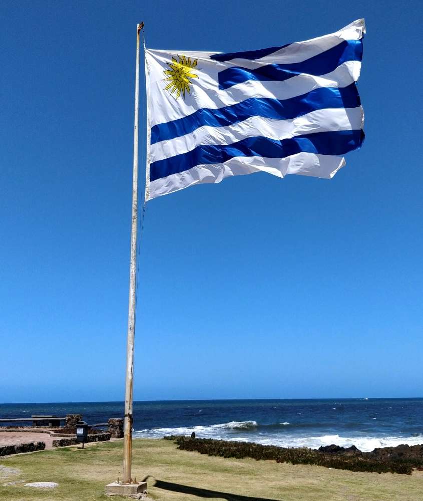 bandeira do uruguai hasteada em frente ao mar, durante o dia em um dos destinos no uruguai