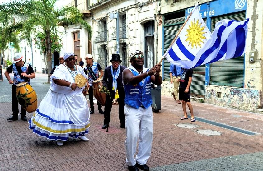durante o dia, pessoas dançando, tocando instrumentos e segurando bandeira do país, em desfile cultural no uruguai
