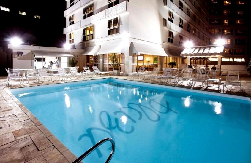espreguiçadeiras ao redor de piscina, durante a noite em área de lazer de Plaza Blumenau Hotel