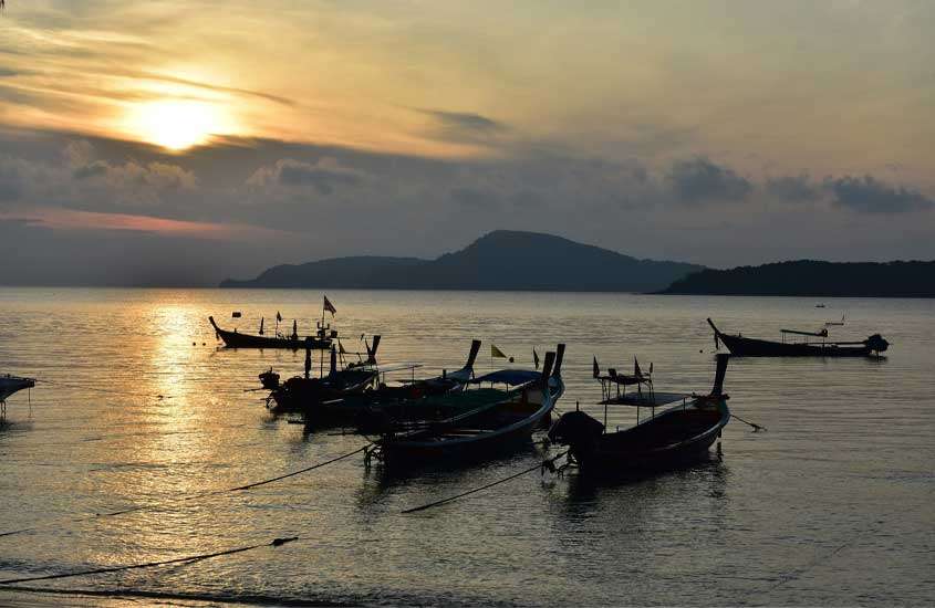 Durante o pôr do sol, paisagem de praia com barcos aportados e montanhas atrás