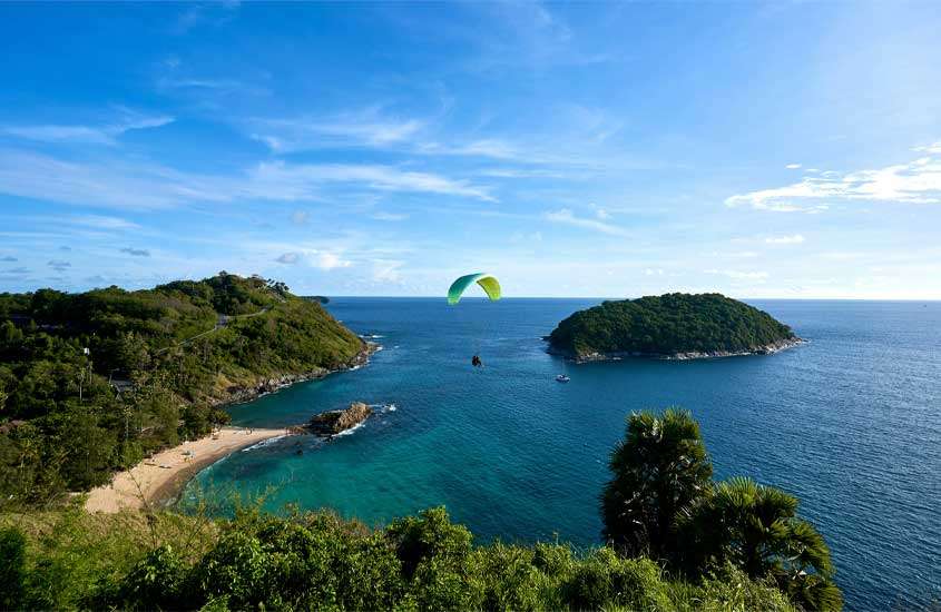 Em um dia de sol, vista aérea de phuket com praia no meio, árvores ao redor, ilha e pessoas voando de paraquedas