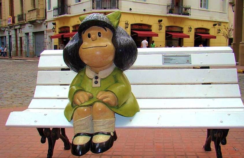 durante o dia, estátua de personagem mafalda, com vestido verde, sentada em banco de praça, durante o dia em rua de buenos aires