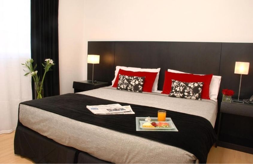 travesseiros, jornais e bandeja com suco e frutas em cima de cama de casal de suíte de Broadway Hotel & Suites