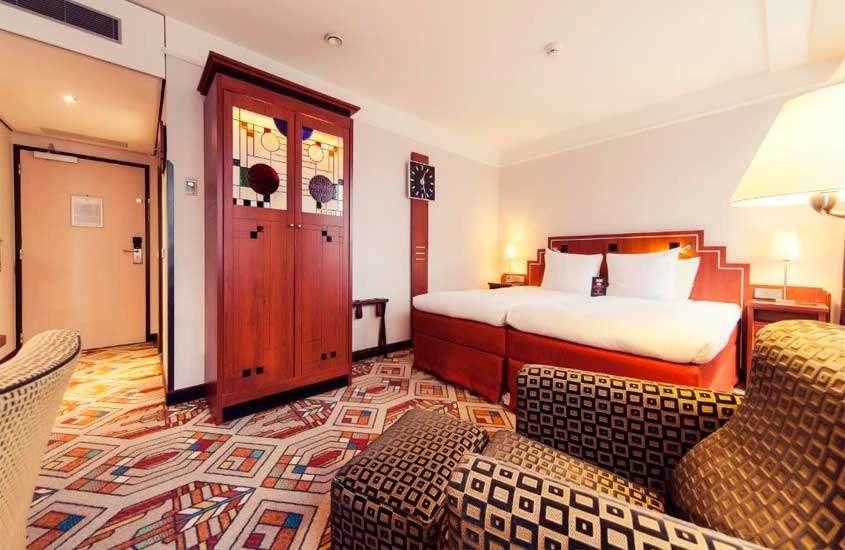 Quarto de hotel com cama de casal, poltrona, armário, relógio retro e piso de carpete