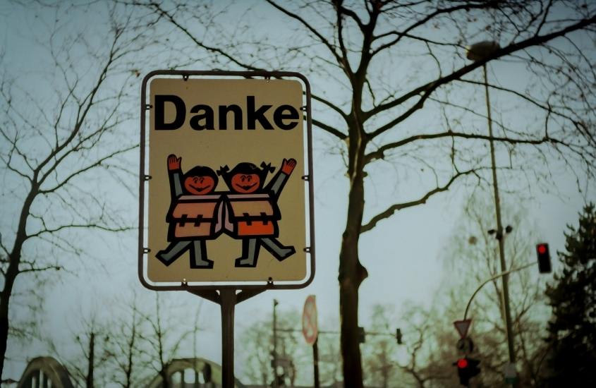 durante o dia, em rua da alemanha, placa onde há escrito 'danke' acima de desenho de duas crianças acenando