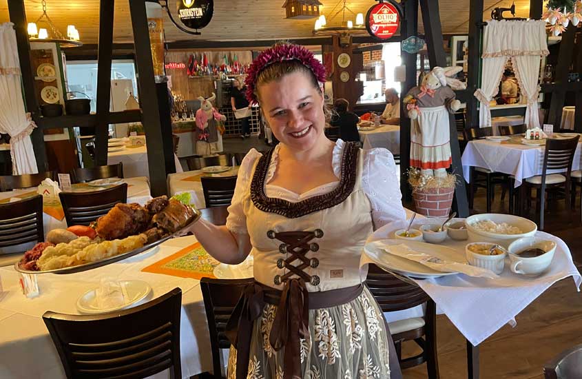 garçonete vestida com roupas típicas alemãs, segura pratos de comida, em um dos restaurantes em pomerode