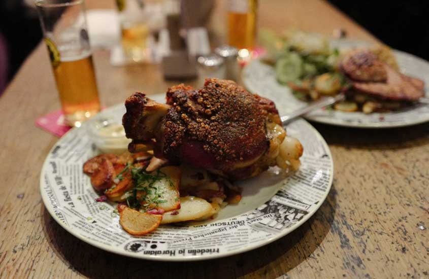 prato branco onde há legumes e carne e copo de cerveja em cima de mesa de madeira
