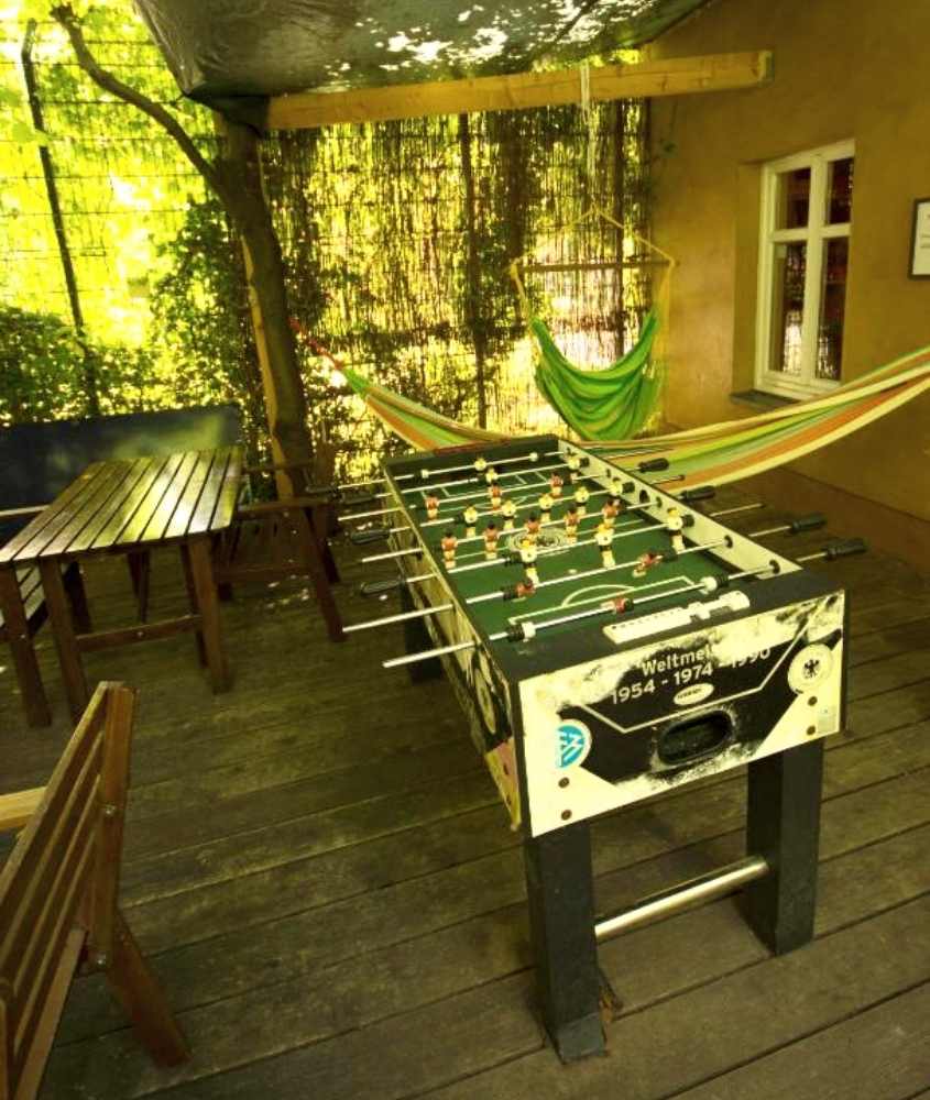 mesa de madeira, redes de descanso e mesa de pebolim, em área de lazer de um dos hostels em berlim, durante o dia