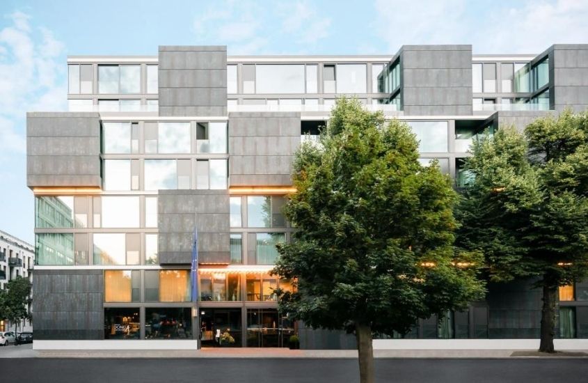 durante o dia, árvores em frente a prédio cinza onde funciona um dos hoteis em berlim alemanha