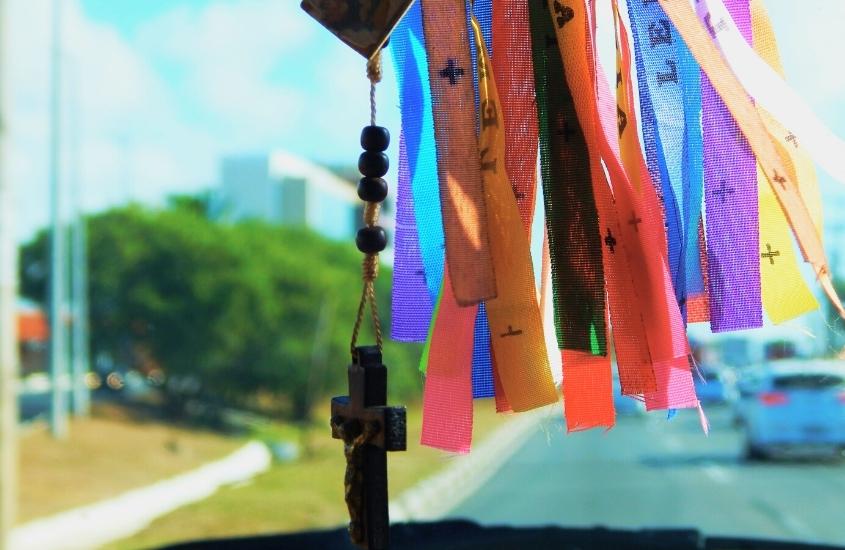 colar com crucifixo de madeira e fitinhas coloridas de senhor do bonfim pendurados em painel de carro, durante o dia em viagem para aracaju