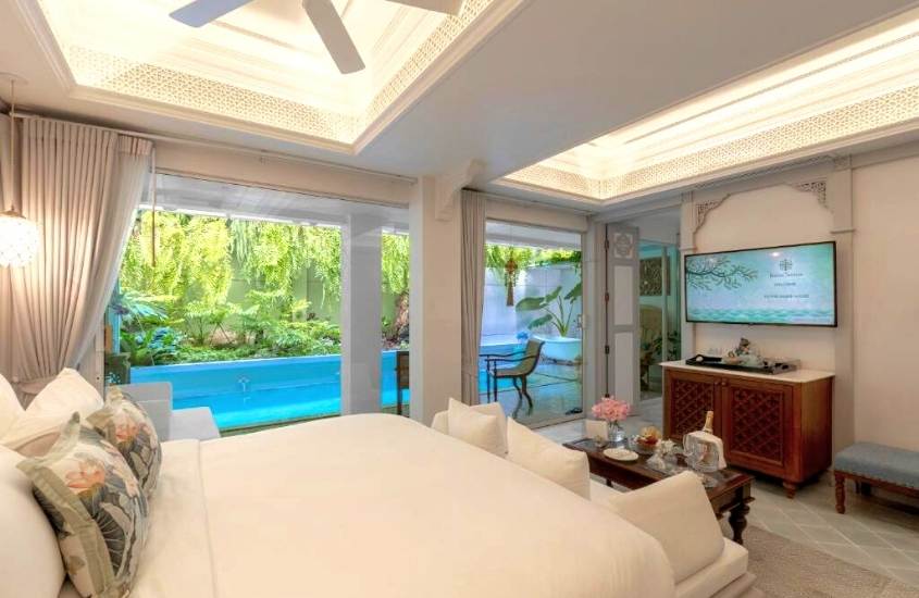 travesseiros em cima de cama de casal, em frente a ampla janela com vista para varanda, onde há piscina, durante o dia em suíte de hotel em chiang mai