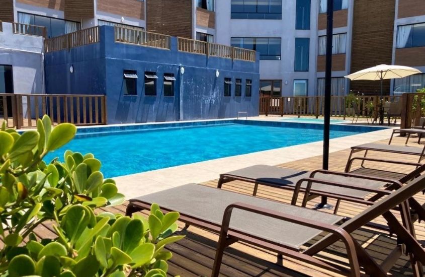 espreguiçadeiras em frente a piscina, durante dia ensolarado em área de lazer de hotel