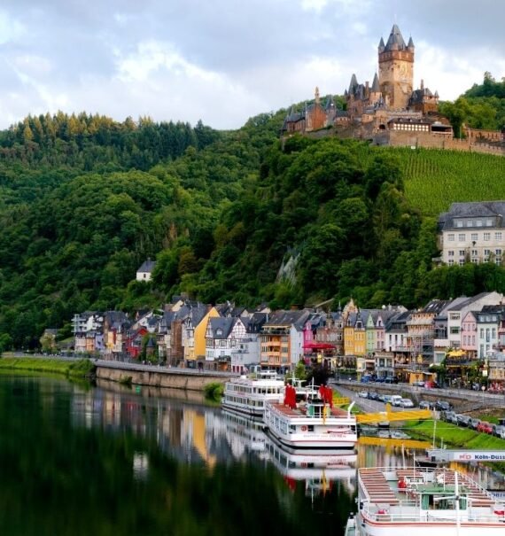 durante o dia, castelo em topo de montanha, e casas coloridas abaixo à beira de lago em uma das cidades da alemanha para visitar