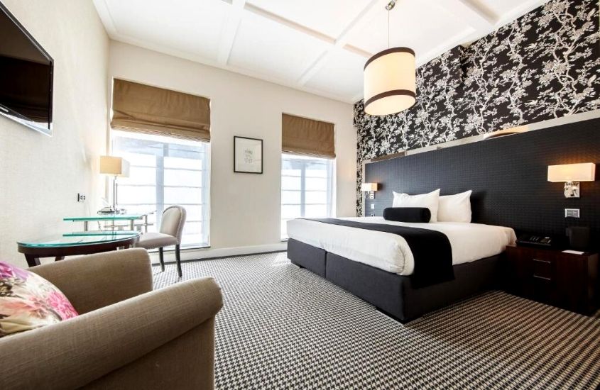 poltrona, cadeiras, mesas e cama de casal, em suite ampla de hotel em amsterdam
